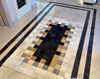 May include: A rectangular rug with a geometric pattern in shades of black, white, gray, and tan. The rug is made of squares of material and is surrounded by a black and white border. The word "LANORRA" is visible in the bottom right corner.
