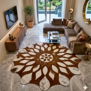 May include: A large, round cowhide rug with a floral design. The rug features a brown and white pattern, with a central geometric design. The rug is placed in a living room with a brown sectional sofa and a wooden entertainment center.