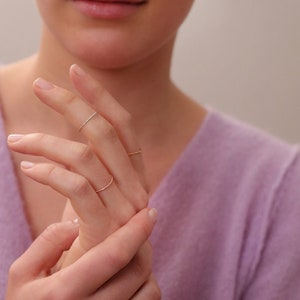 Könnte beinhalten: Eine Hand trägt drei dünne goldene Ringe. Die Ringe sind übereinander auf dem Finger und sehr zart.