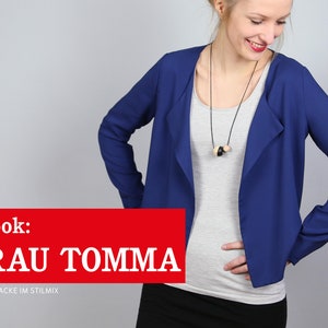 Pode incluir: Uma mulher vestindo um blazer azul com gola drapeada e uma camiseta branca por baixo. O blazer tem mangas compridas e um caimento relaxado. A mulher est&aacute; usando uma saia preta e um colar com contas de madeira. O texto "e-book: FRAU TOMMA L&Auml;SSIGE JACKE IM STILMIX" &eacute; exibido na parte inferior da imagem.
