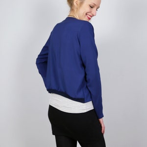 Pode incluir: Uma jaqueta bomber azul marinho cropped com mangas compridas e bainha de malha.