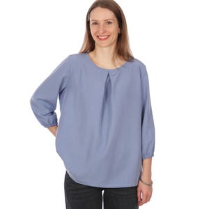 Pu&ograve; includere: Camicetta azzurra con scollo tondo e maniche a tre quarti. Le maniche sono raccolte ai polsini. La camicetta ha un dettaglio a pieghe sul davanti e un orlo curvo. La modella indossa jeans neri.