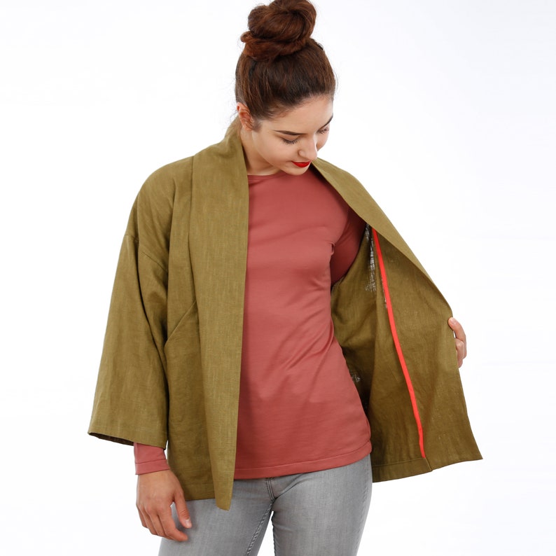 Peut inclure: Une veste en lin vert avec une doublure rouge. La veste a un col large et des manches longues. La veste est ouverte et la doublure est visible.