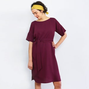 May include: A burgundy midi dress with a self-tie belt and short sleeves. The dress has a simple, elegant design.
