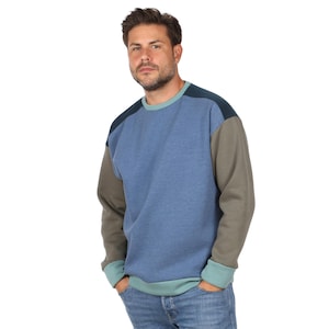 Puede incluir: Una sudadera de manga larga con diseño de bloques de color que presenta un panel central azul, mangas verde oliva, detalles en los hombros azul marino oscuro y un cuello redondo, puños y dobladillo acanalados en color verde azulado claro.