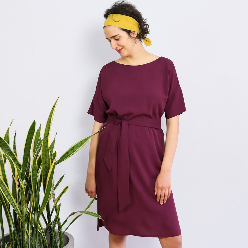 May include: A burgundy midi dress with a short sleeve and a self-tie belt. The dress has a round neckline and is made of a soft, flowing fabric.