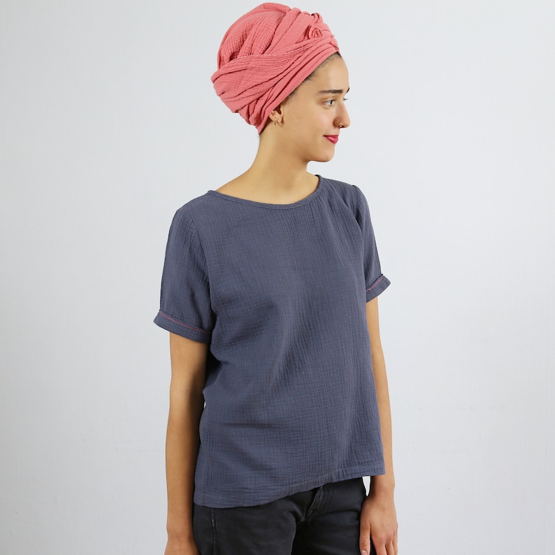 May include: A woman wearing a gray, short-sleeved t-shirt with a pink turban on her head.