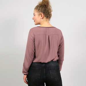 Könnte beinhalten: Eine mauvefarbene Bluse mit langen Ärmeln, V-Ausschnitt und einer einzigen Falte im Rücken.