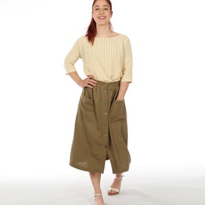 Puede incluir: Una mujer con una camisa de rayas amarillas y una falda marrón con botones y bolsillos.