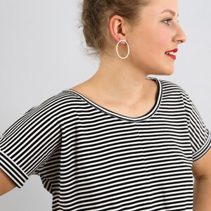 May include: A short-sleeved shirt featuring a horizontal black and white striped pattern with a round neckline and a center seam detail. The garment is paired with a simple, thin, circular silver hoop earring worn in the earlobe.