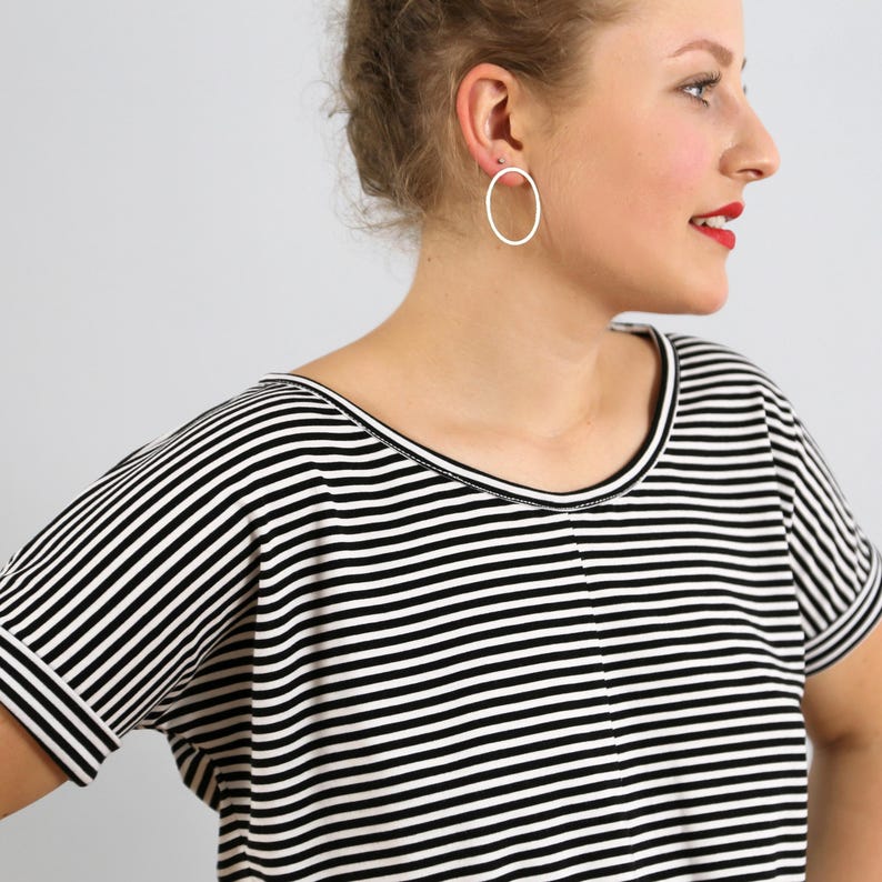 May include: A short-sleeved shirt featuring a horizontal black and white striped pattern with a round neckline and a center seam detail. The garment is paired with a simple, thin, circular silver hoop earring worn in the earlobe.
