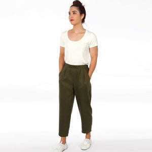 Pode incluir: Uma mulher vestindo uma camiseta branca de gola redonda e calças verde-oliva de cintura alta com pregas. Ela está de pé com as mãos nos bolsos e olhando para a esquerda.