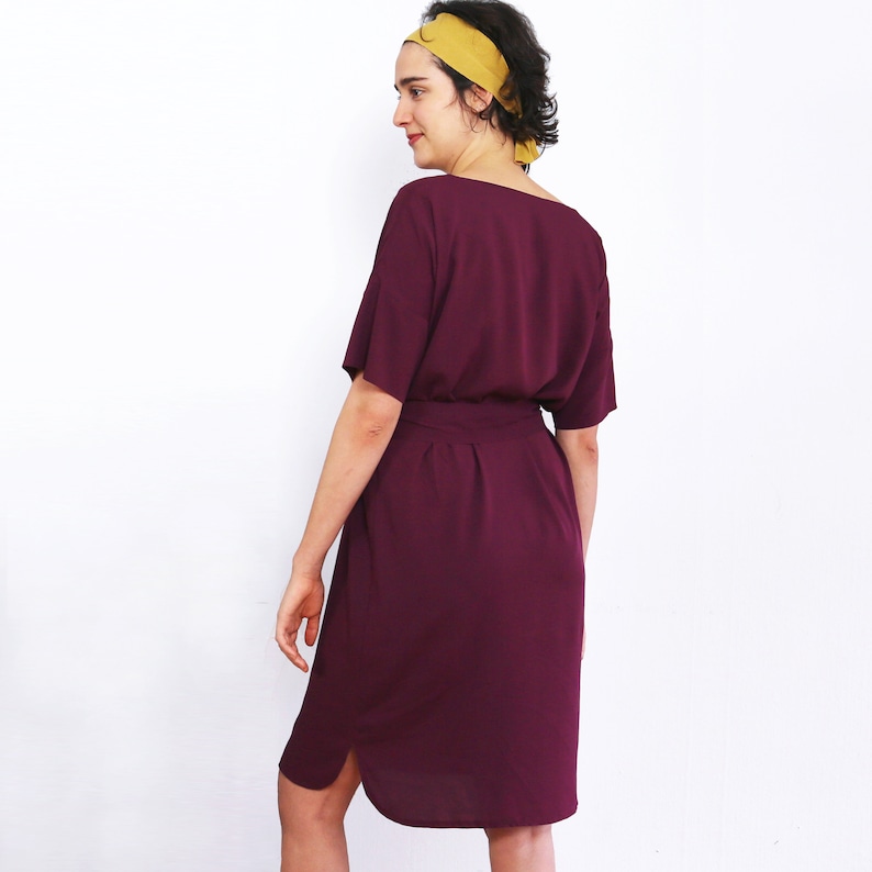 May include: A burgundy midi dress with a short sleeve and a tie belt. The dress has a scoop neck and a slightly flared skirt.