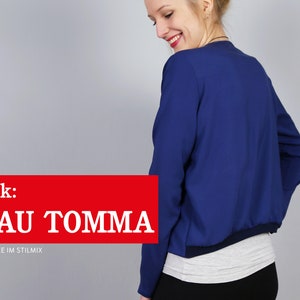 Pode incluir: Uma mulher vestindo uma jaqueta bomber azul com uma camisa branca por baixo. O texto "e-book: FRAU TOMMA L&Auml;SSIGE JACKE IM STILMIX" &eacute; exibido em vermelho.