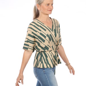 Könnte beinhalten: Eine beige und grüne gemusterte Bluse mit V-Ausschnitt und einer Schleife an der Taille.