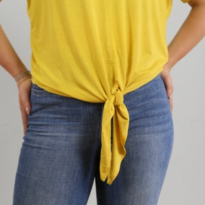 May include: A yellow shirt tied at the waist with a knot, worn over blue jeans.
