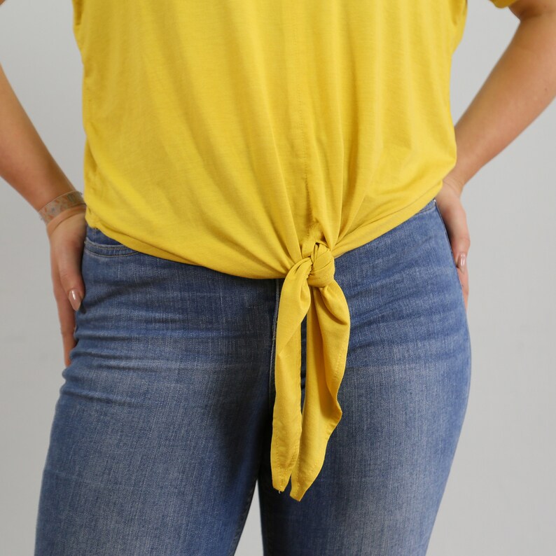 May include: A yellow shirt tied at the waist with a knot, worn over blue jeans.