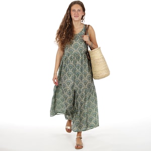 Peut inclure: Une femme porte une robe longue verte à motifs avec un col en V et une jupe à volants. Elle porte un sac fourre-tout en paille avec des lanières en cuir marron et des sandales dorées. La robe présente un motif répétitif en forme d'éventail.