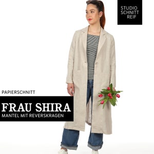 Op de afbeelding: Een beige linnen jas met een enkele knoopsluiting en een klepzak. De jas heeft een kraag en lange mouwen. Het model draagt ​​een blauwe jeans en een gestreept shirt. De tekst "FRAU SHIRA" en "MANTEL MIT REVERSKRAGEN" is zichtbaar op de afbeelding.