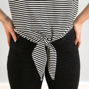 May include: A black and white striped shirt tied at the waist with a bow. The shirt is worn with black jeans.