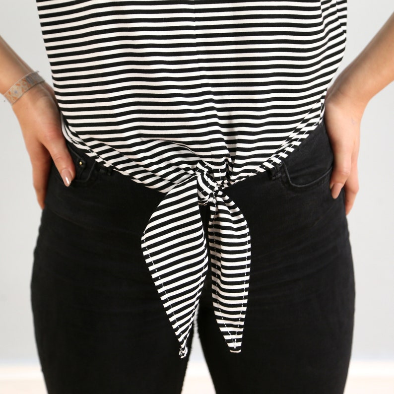 May include: A black and white striped shirt tied at the waist with a bow. The shirt is worn with black jeans.