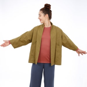 Peut inclure: Une femme portant une veste en lin vert sur un t-shirt rose et un pantalon bleu. La veste a une coupe ample et un col large.