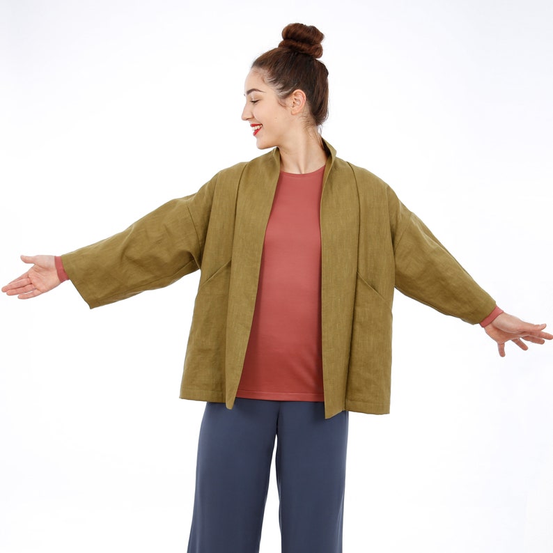 Peut inclure: Une femme portant une veste en lin vert sur un t-shirt rose et un pantalon bleu. La veste a une coupe ample et un col large.