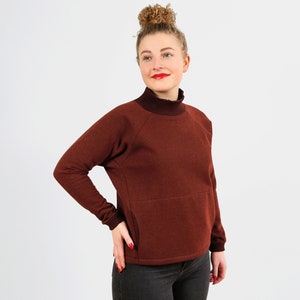 May include: A maroon turtleneck sweater with a long sleeve and a pocket on the front. The sweater is made of a soft, comfortable fabric.