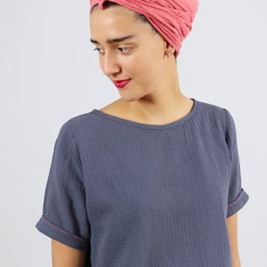 May include: A blue cotton t-shirt with a scoop neck and short sleeves. The sleeves have a pink stitch detail.