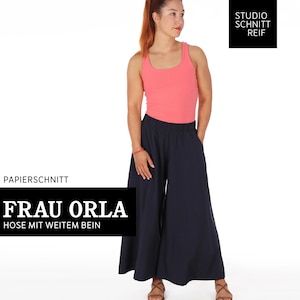 May include: A sewing pattern for wide-leg trousers called "Frau Orla" by Studio Schnitt Reif. The pattern is for a pair of wide-leg trousers with a high waist and a relaxed fit. The pattern is shown on a model wearing a pink tank top and the trousers.