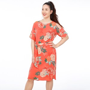 May include: A coral-colored midi dress with a floral print and a self-tie belt. The dress has short sleeves and a round neckline.