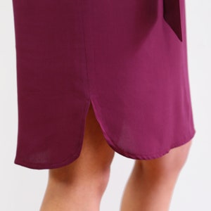 May include: A burgundy midi dress with a side slit and a curved hemline.