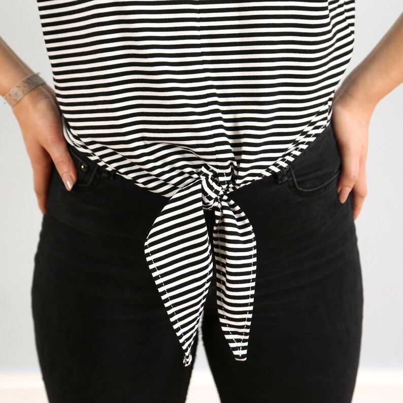 May include: A black and white striped shirt tied at the waist with a bow. The shirt is worn over black jeans.