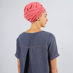 May include: A woman wearing a coral pink turban and a dark blue, short-sleeved shirt with pink stitching.