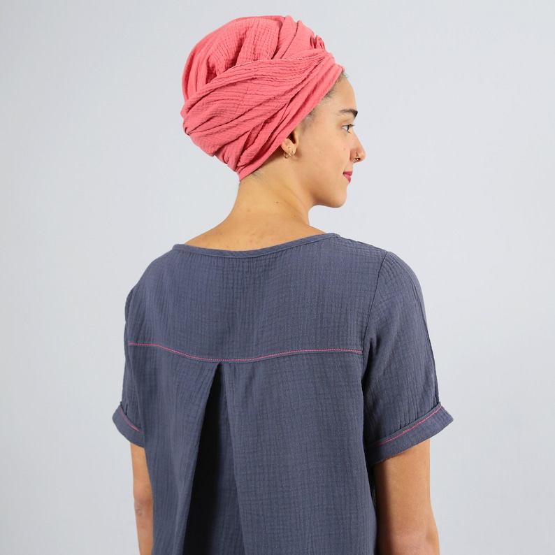 May include: A woman wearing a coral pink turban and a dark blue, short-sleeved shirt with pink stitching.