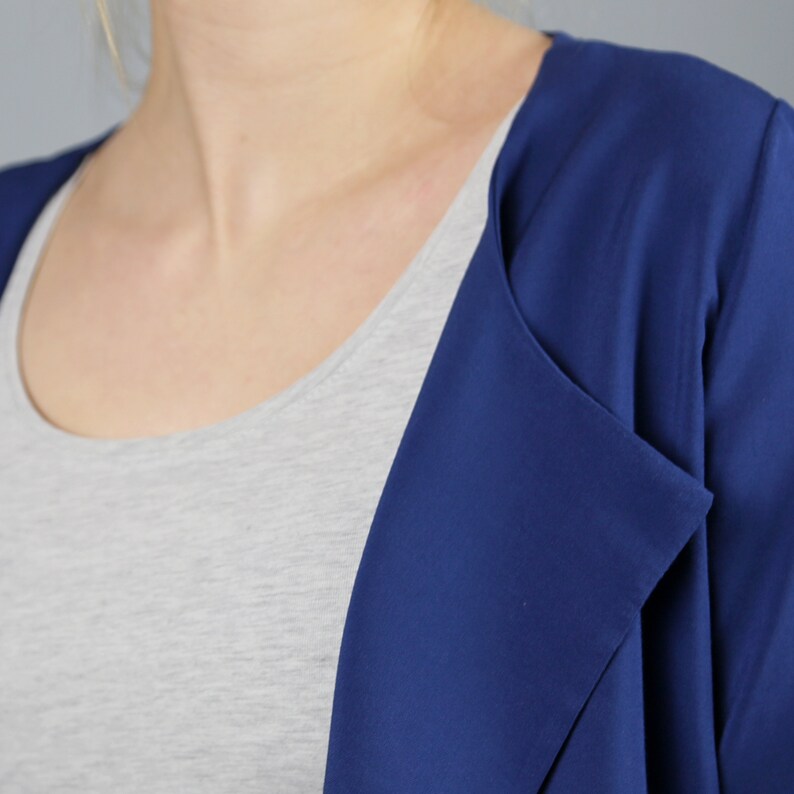 Pode incluir: Um close-up de um blazer azul marinho com gola drapeada. O blazer &eacute; feito de um tecido liso e leve.