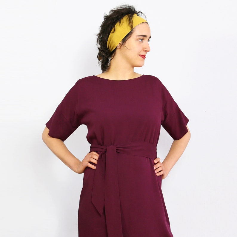 May include: A woman wearing a maroon dress with a self-tie sash and a mustard yellow headband.