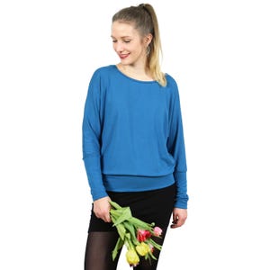 Op de afbeelding: Een blauwe top met lange mouwen, een brede ronde halslijn en een aansluitende boord aan de onderkant. Het kledingstuk heeft losse, gedrapeerde mouwen die smaller toelopen bij de polsen, wat zorgt voor een ontspannen silhouet. De stof is effen blauw.