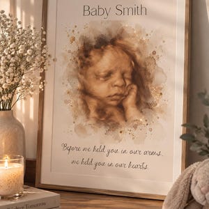 May include: A framed print featuring a sepia-toned watercolour-style ultrasound image of a baby. The text reads Baby Smith at the top and Before we held you in our arms, we held you in our hearts at the bottom. The artwork has gold paint splatters.
