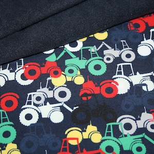 Può includere: Un tessuto blu navy con un motivo ripetuto di trattori bianchi, rossi, verdi e gialli. I trattori sono tutti rivolti nella stessa direzione e hanno design diversi.