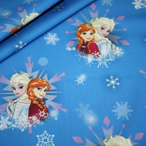 Könnte beinhalten: Blauer Stoff mit einem sich wiederholenden Muster von Elsa und Anna aus Frozen und Schneeflocken. Das Design zeigt die Charaktere und Schneeflocken und schafft ein winterliches Thema. Geeignet für verschiedene Bastelprojekte.