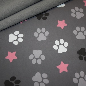 Könnte beinhalten: Grauer Stoff mit einem sich wiederholenden Muster aus Pfotenabdrücken in Weiß, Grau und Schwarz sowie rosa Sternen.