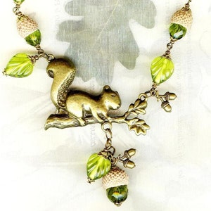 Collier ECUREUIL des CHÊNES bronze avec coupelles naturelles de GLANDS perles en cristal et feuilles en verre olivine Active image 1