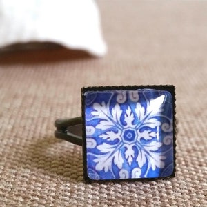 Op de afbeelding: Een vierkante ring met een blauw en wit gepatroneerd tegelontwerp. De ring is gemaakt van zwart metaal.