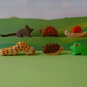 Könnte beinhalten: Ein Set aus Holztierfiguren, darunter eine Maus, eine Schildkröte, eine Schnecke, ein Igel und ein Frosch. Die Figuren sind in leuchtenden Farben bemalt und haben realistische Details.