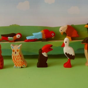 Könnte beinhalten: Ein Set aus neun Holztierfiguren, darunter ein rot-blauer Papagei, ein rot-weißer Vogel, eine braun-weiße Eule, ein rot-weißer Vogel, eine braun-weiße Eule, ein schwarz-weißer Pinguin, ein schwarz-weißer Tukan, ein braun-weißer Vogel und ein schwarz-weißer Vogel.