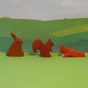 Könnte beinhalten: Drei Holztierfiguren: ein Kaninchen, ein Eichhörnchen und ein Fuchs. Alle sind in einem einheitlichen Rot lackiert.