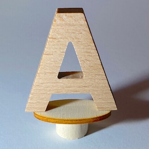 Könnte beinhalten: Ein Holzbuchstabe A mit einem Ausschnitt in Form des Buchstabens A. Der Buchstabe ist auf einem Holzsockel montiert.