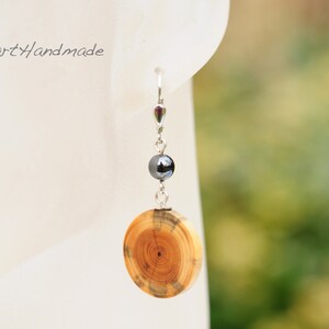 May include: Silver dangle earrings with a round wooden charm and a black bead. The wooden charm has a wood grain pattern.