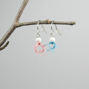 May include: A pair of dangle earrings with a pearl bead and a small figure made of curled paper. One figure is pink and the other is blue.